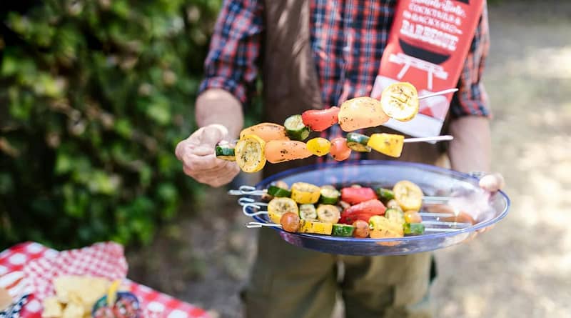 Person Holding a Platter of Sliced Fruits and Vegetables on Skewers