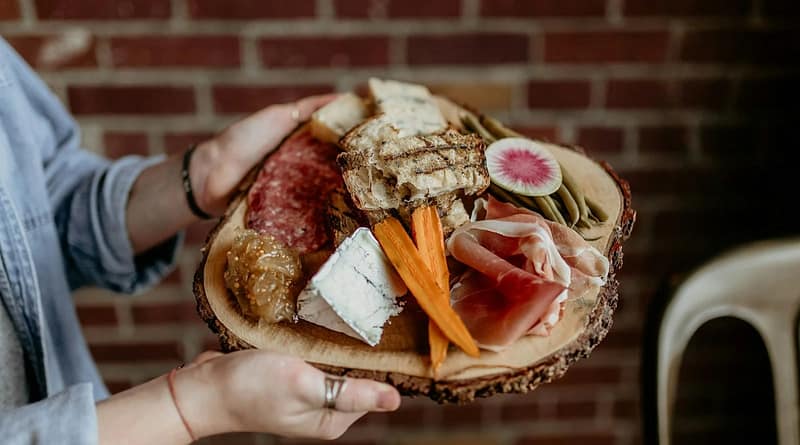 a person holding a platter of meats and cheeses